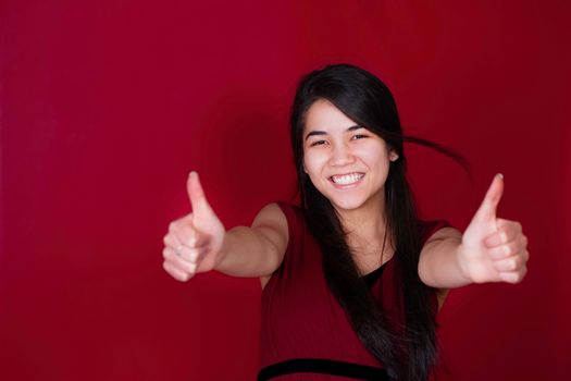 Beautiful biracial teen girl with thumbs up on red background
