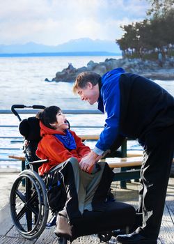 Handsome father talking with disabled biracial son outdoors by lake