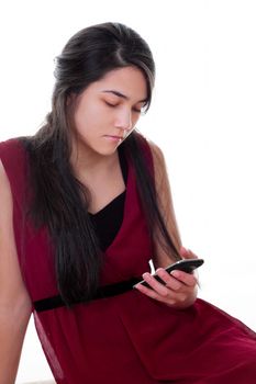 Beautiful biracial teen girl in red dress looking at cell phone in hand, texting or reading