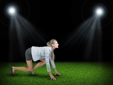 Businesswoman standing in running start pose at green grass court illuminated by two spotlights, looking ahead, smiling