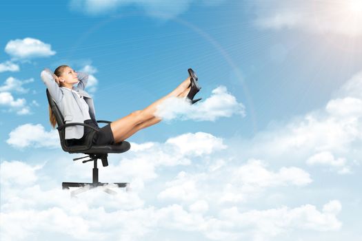 Businesswoman leaning back in office chair standing on cloud, with her feet up on smaller cloud, looking at light shining from above