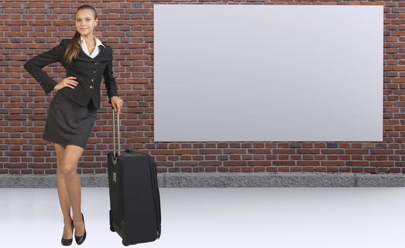 Businesswoman with travel bag posing against red brick wall with blank white banner, looking at camera, smiling