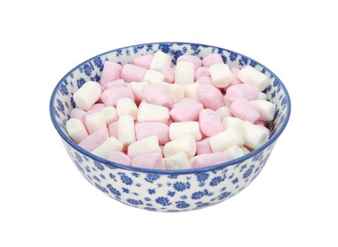 Pink and white mini marshmallows in a blue and white porcelain bowl with a floral design, isolated on a white background