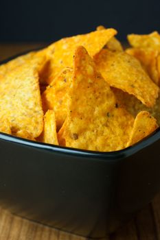 Nacho cheese flavored tortilla chips in a dark bowl on a wooden table.