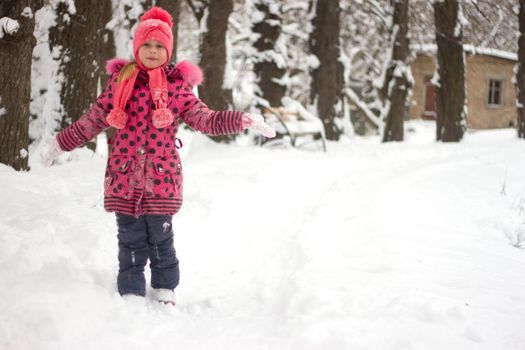 Little girl in winter pink hat in snow.