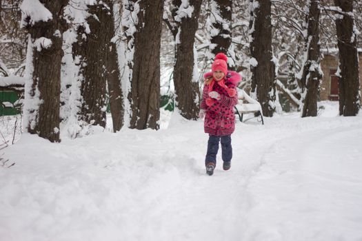 Little girl in winter pink hat in snow.