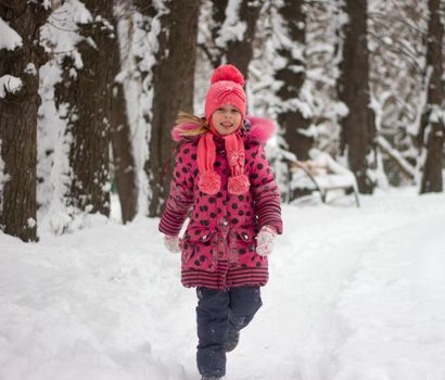 Little girl in winter pink hat in snow.