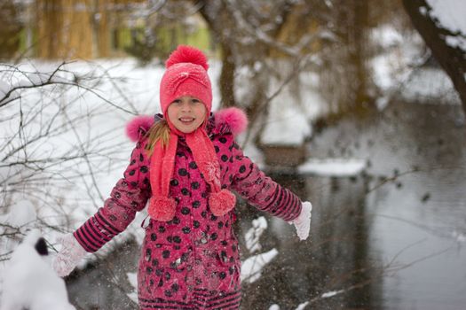 Little girl in winter pink hat in snow.