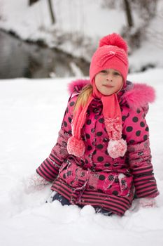 Little girl in winter pink hat in snow.