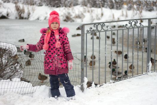 Little girl in winter pink hat in snow.