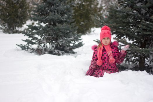 Little girl in winter pink hat in snow.