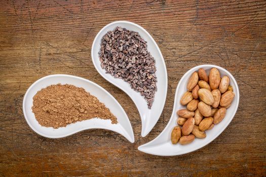 cacao beans, nibs and powder - top view of teardrop shaped bowls against rustic wood