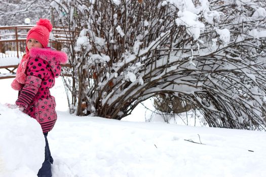 Little girl in winter pink hat in snow.