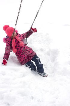 Adorable girl having fun on a swing on beautiful winter day