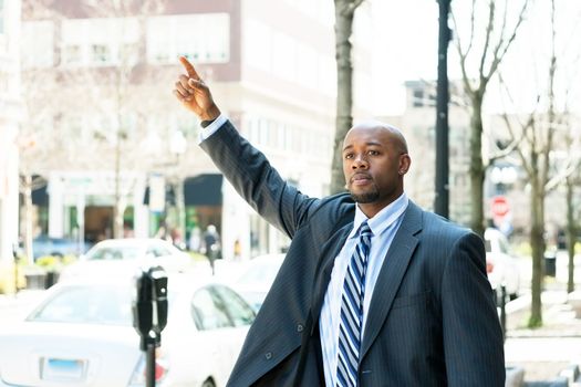 An African American business man raises his hand to hail a cab in the city.