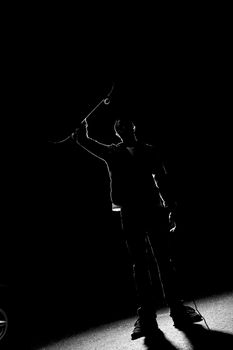 A backlit skateboarder guy holding up his skateboard deck under dramatic rim lighting.