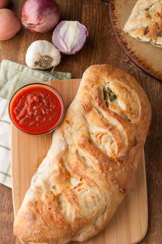 Homemade stromboli or stuffed bread with broccoli potatoes garlic onions and mozzarella cheese along with a side of marinara dipping sauce.