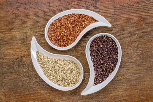 white, red and black quinoa grain - top view of teardrop bowls against rustic wood