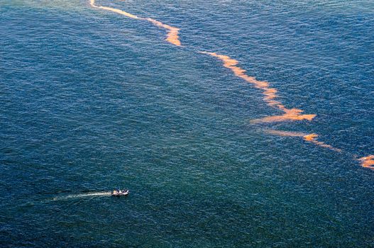 CAPE TOWN, SOUTH AFRICA - DECEMBER 20TH, 2014: A boat with unidentified people approaches pollution in the sea at Gordons Bay near Cape Town
