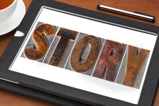 story word in vintage letterpress wood type printing blocks on a digital tablet with a cup of tea