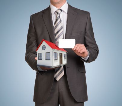 Businessman in suit hold empty card and small house. Blue background