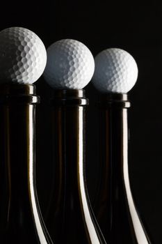 Silhouettes of elegant wine bottles with golf balls on a black background