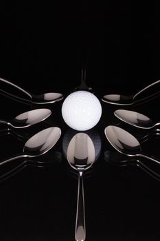 Teaspoons and white golf ball on the black glass desk