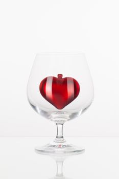 Red heart inside a glass of cognac on a glass plate