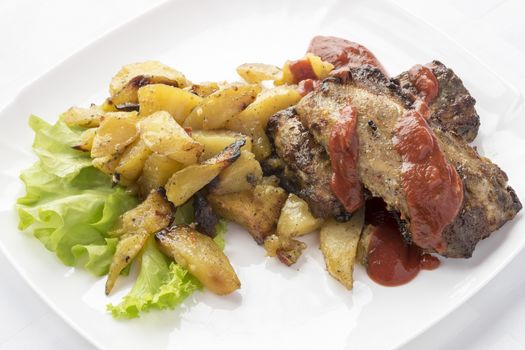 Lettuce ,fried potatoes,pork ribs lie on the plate.