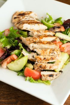 Freshly prepared grilled chicken chef style salad with tomato cucumber green pepper and romaine lettuce.