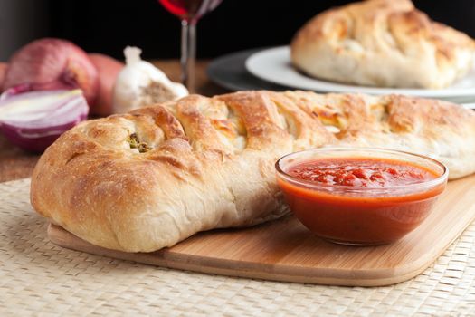 Homemade stromboli or stuffed bread with broccoli potatoes garlic onions and mozzarella cheese along with a side of marinara dipping sauce.