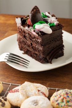 Decadent slice of chocolate cake with iced flowers and chocolate covered strawberries on a plate with a fork.