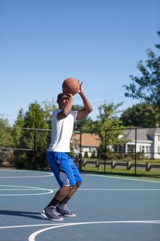 Basketball player shooting the ball at the basket on an outdoor court.