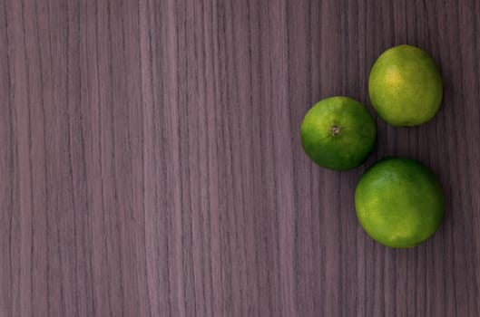 A heap of three green lemons over wood