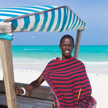 Traditonaly dressed black man on the beach. Maasai warrior on picture perfect tropical sandy beach on Zanzibar, Tanzania, East Africa.