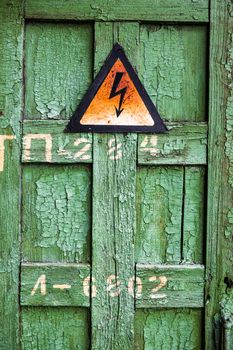 Old rusty warning high voltage sign on cracked green wooden surface