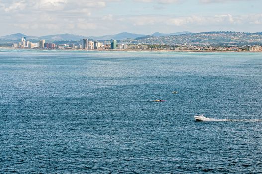 CAPE TOWN, SOUTH AFRICA - DECEMBER 20, 2014: A speed boat and canoes with unidentified people in the sea at Gordons Bay near Cape Town. The Strand  and Somerset West are seen across the sea
