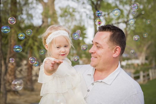 Affectionate Father Holding Cute Baby Girl Enjoying Bubbles Outside at the Park.