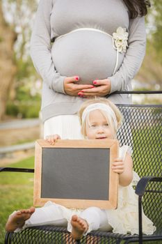 Pregnant Mom Behind Cute Baby Girl Sitting in Chair Holding Blank Blackboard.