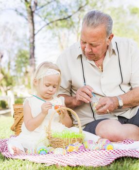 Loving Grandfather and Granddaughter Coloring Easter Eggs Together on Picnic Blanket At The Park.