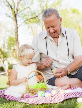 Loving Grandfather and Granddaughter Coloring Easter Eggs Together on Picnic Blanket At The Park.