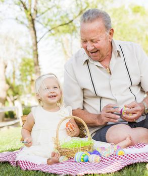 Loving Grandfather and Granddaughter Coloring Easter Eggs Together on Picnic Blanket At The Park.