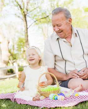 Loving Grandfather and Granddaughter Coloring Easter Eggs Together on Picnic Blanket At The Park.