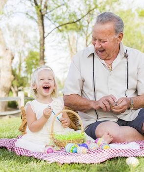 Loving Grandfather and Granddaughter Coloring Easter Eggs Together on Picnic Blanket At The Park.