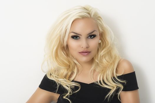 Glamorous blond woman with shoulder length curly hair in an elegant black cocktail dress looking directly at the camera with a serious expression