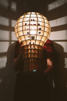 Hanging, wooden light shade lamp with bulb in hands
