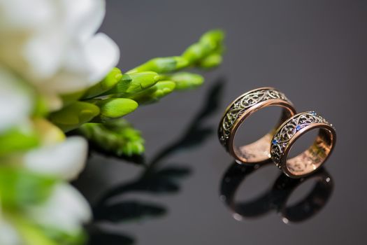 Two wedding rings in infinity sign with bouquet on black background. Love concept.