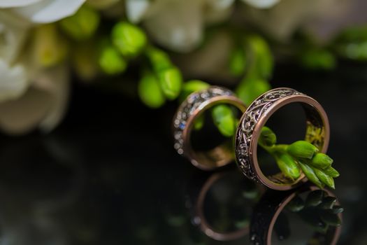 Two wedding rings in infinity sign with bouquet on black background. Love concept.