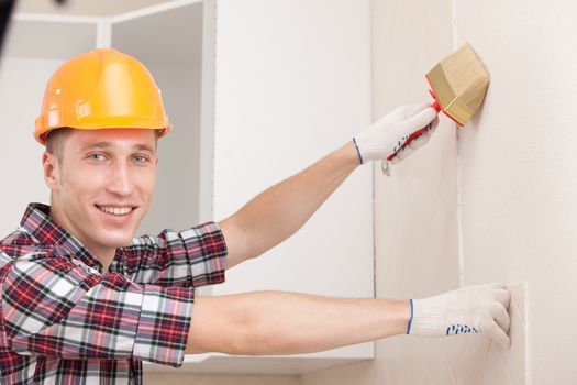 smiling worker with paint brush prepares the wall for wallpapering