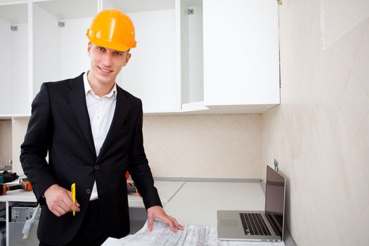 engineer with blueprints of object and laptop in interior of new apartment